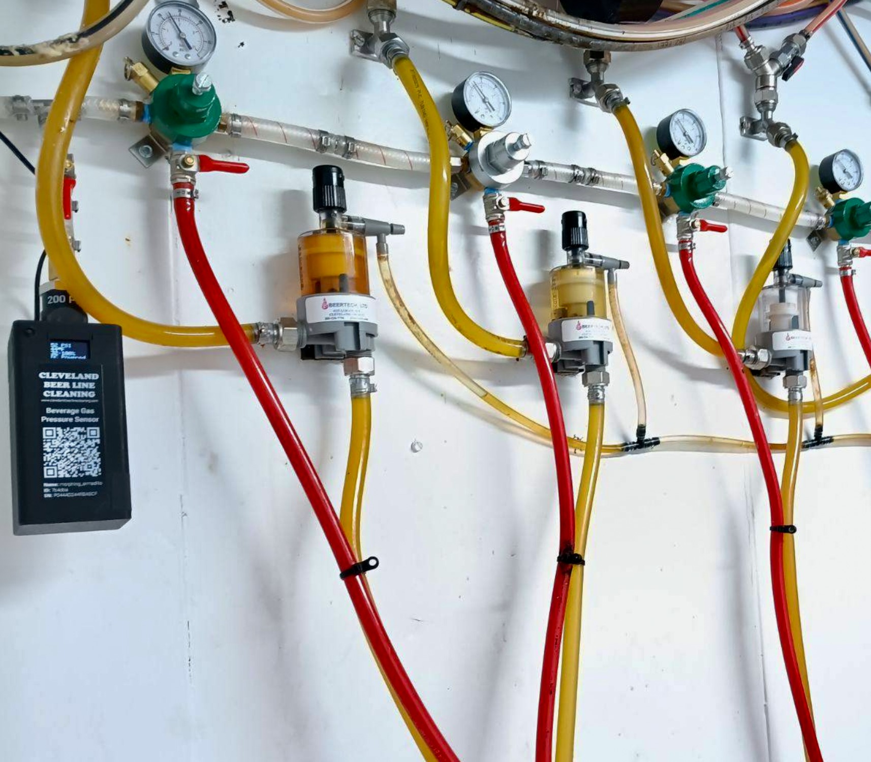 A Barkeep beverage gas pressure sensor installed on a commercial beer-gas regulator manifold with rows of gauges and red and yellow gas lines at a customer site.
