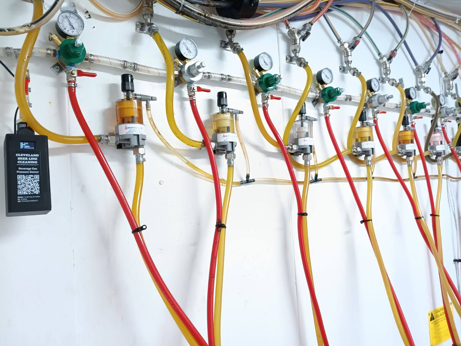 A Barkeep beverage gas pressure sensor installed on a commercial beer-gas regulator manifold with rows of gauges and red and yellow gas lines at a customer site.